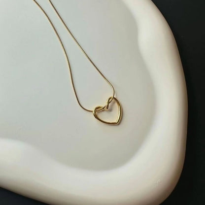 Twisted Heart Necklace laid on a white ceramic plate – elegant sculpted heart pendant and snake chain